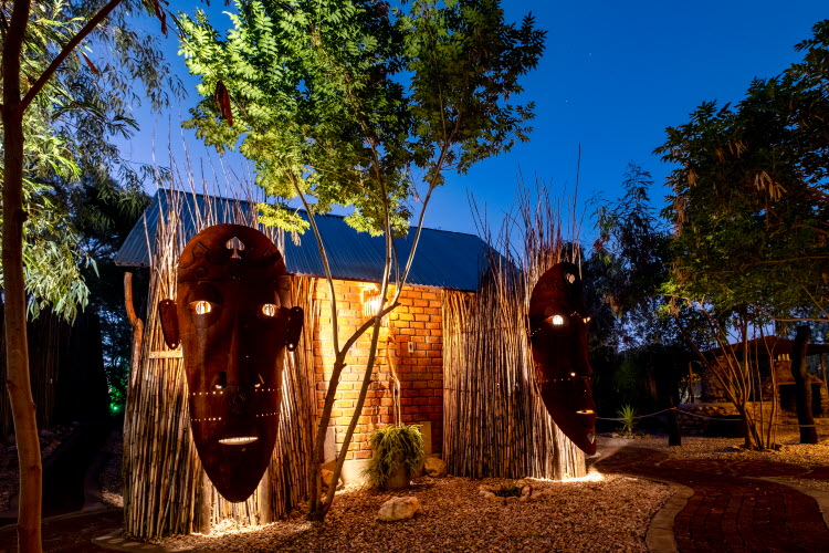 UrbanCamp Windhoek – illuminated African masks in the leafy camp garden