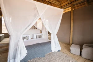 Bed beneath a mosquito net in a thatched Damaraland Camp suite