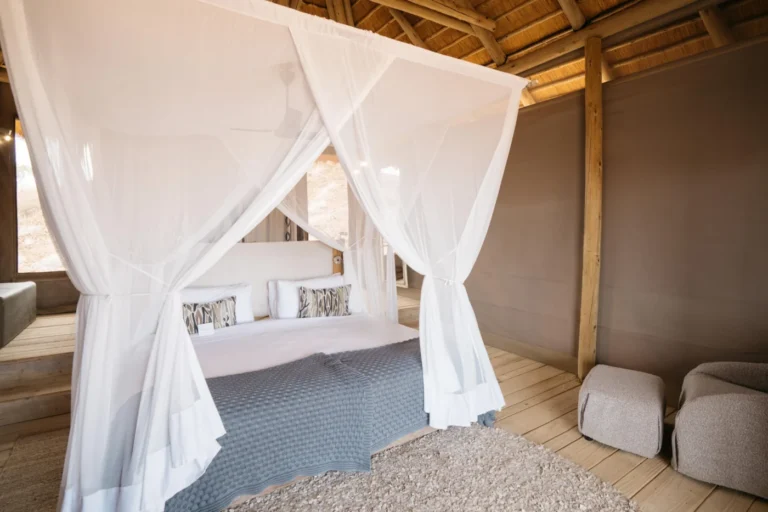 Bed beneath a mosquito net in a thatched Damaraland Camp suite