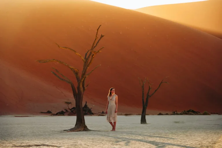 Visitor among dead camelthorn trees and red dunes at Deadvlei